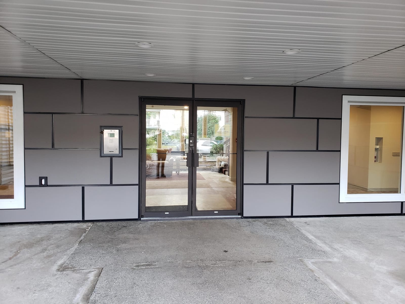 Grey panel siding with black reveal trim around a glass entrance